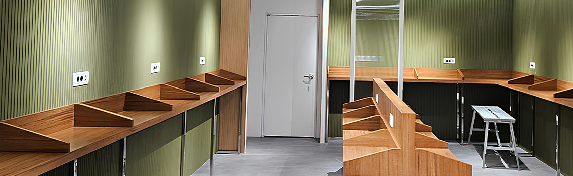 Modern study area with wooden carrel desks against olive green corrugated walls under bright track lighting.
